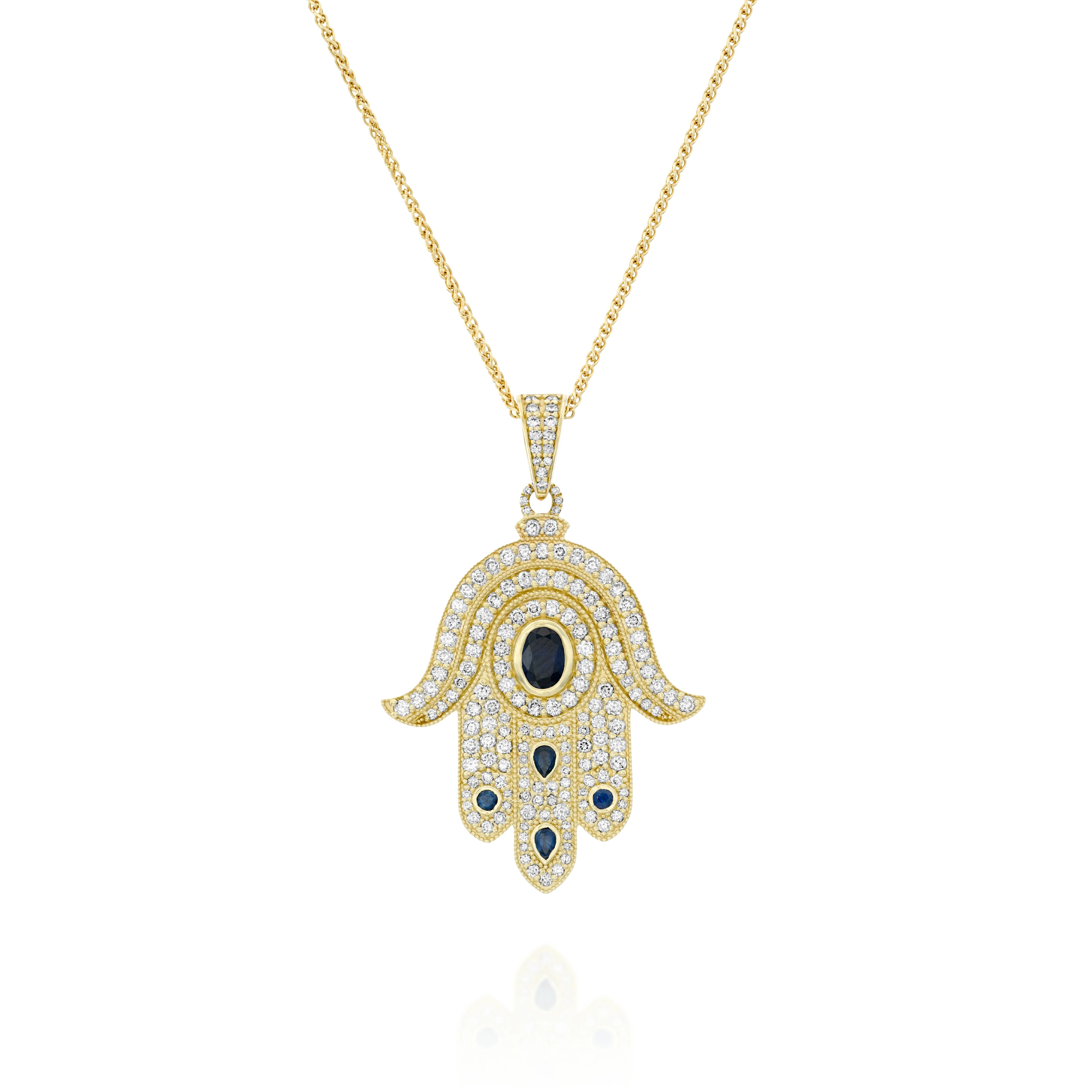 A yellow gold Hamsa pendant set with round brilliant diamonds and
sapphires. At the heart of the pendant lies a round sapphire symbolizing
the compassionate Guardian Eye ( against the Evil Eye ) , that always
carefully watches over and protects us. The fusion of the numerous
precious stones with the traditional Hamsa shape creates a pendant that
captivate every heart.